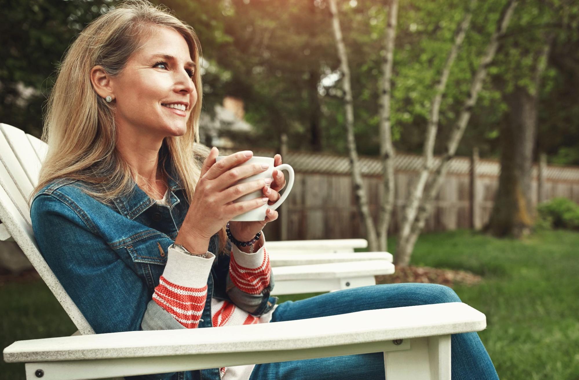 Woman sitting outdoors in a patio chair holding a mug, relaxing and decompressing during a stressful day.