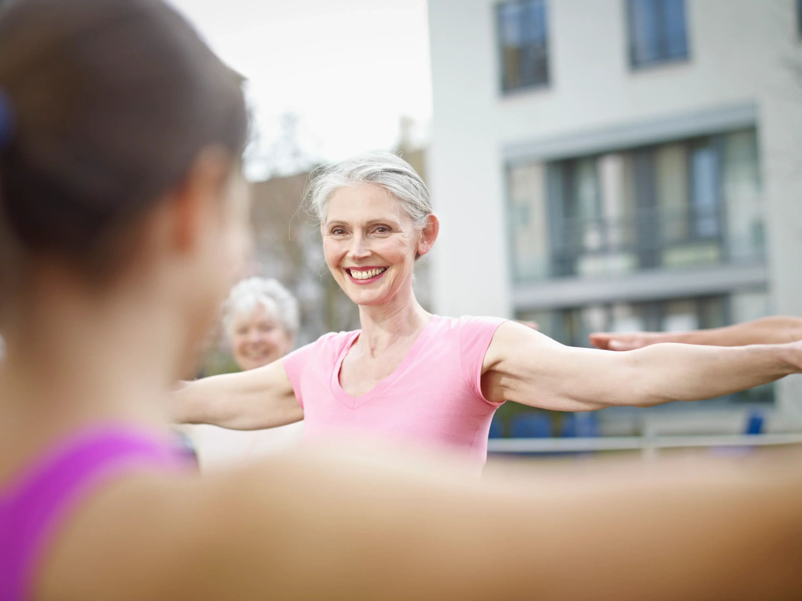 Smiling midlife woman doing a mobility exercise in a group fitness session for menopause transition coaching.