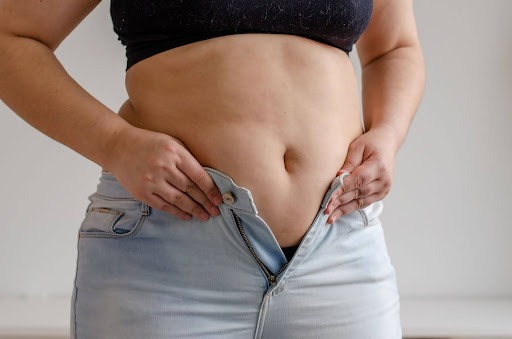 Close-up of a woman’s midsection as she tries to zip up tight jeans, illustrating midlife weight gain or menopause belly changes.