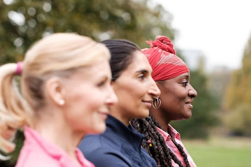 Side profile of three women outdoors, smiling during a group fitness or wellness activity.