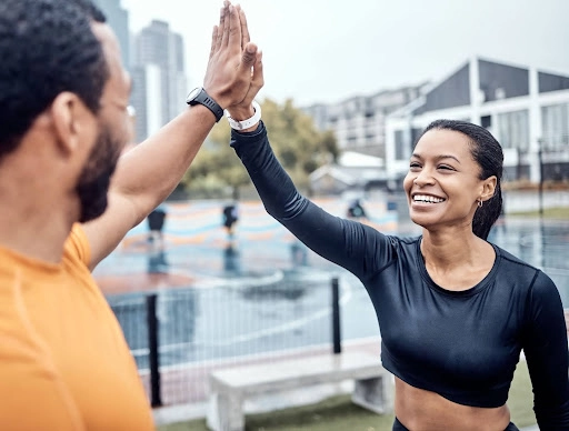 Smiling workout partners high-fiving outdoors after training, representing accountability and celebrating progress in midlife fitness goals.