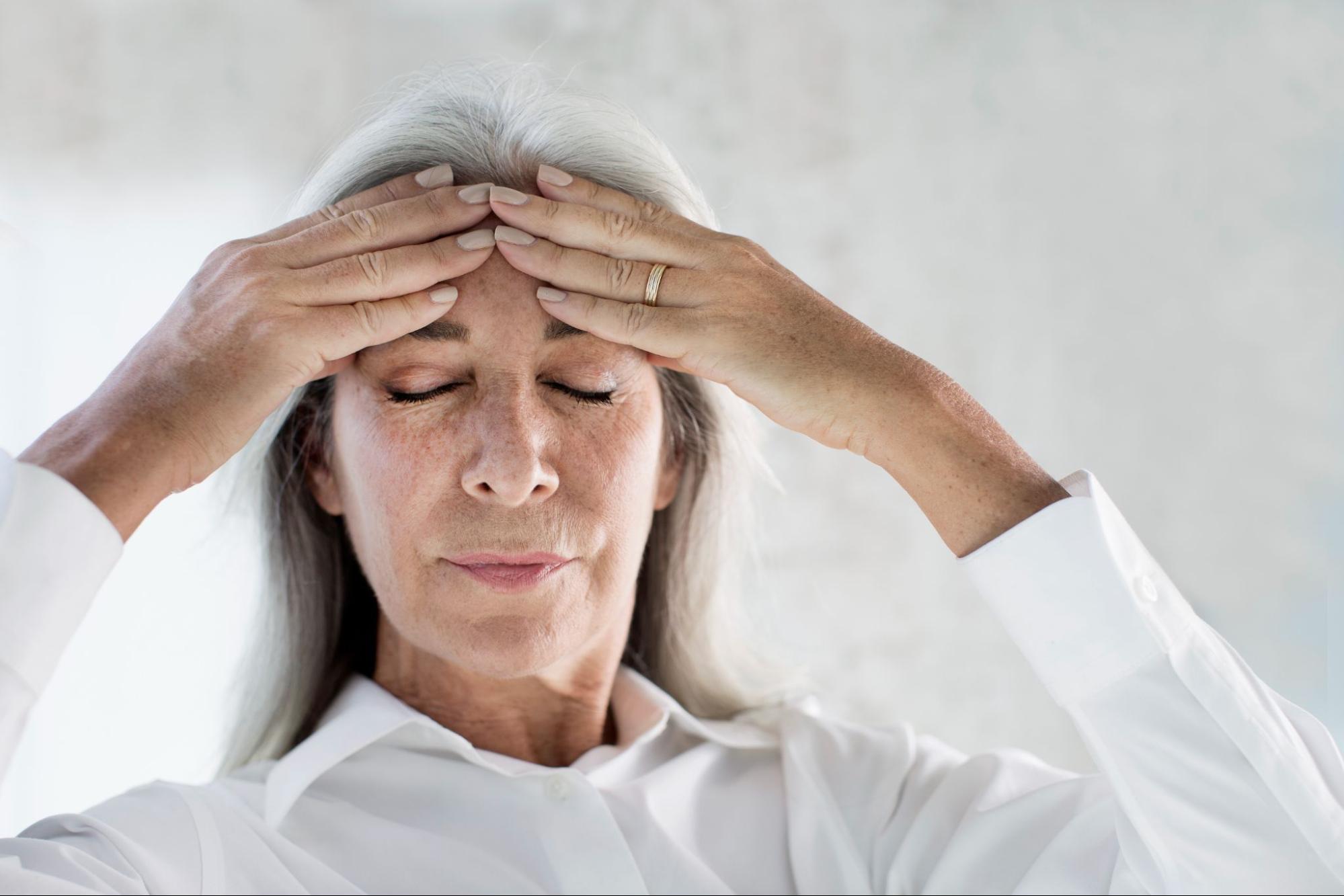 An elderly woman holding her forehead, experiencing a headache or deep thought, symbolizing the challenges of cognitive shifts like brain fog.