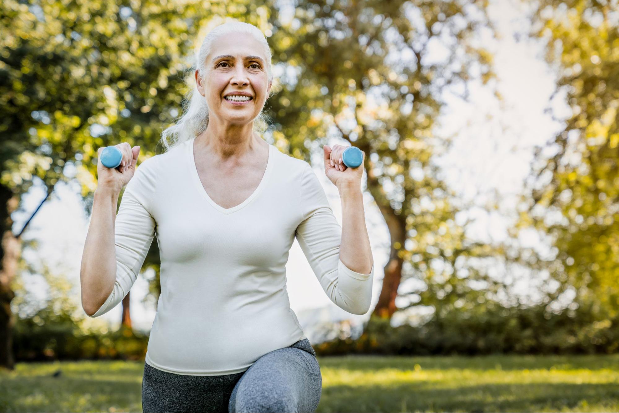 Senior woman exercising outdoors with dumbbells, demonstrating strength training for health and wellness.