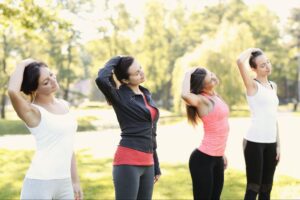 A group of women performing neck stretches outdoors, demonstrating a fitness routine to support bone health and overall strength.