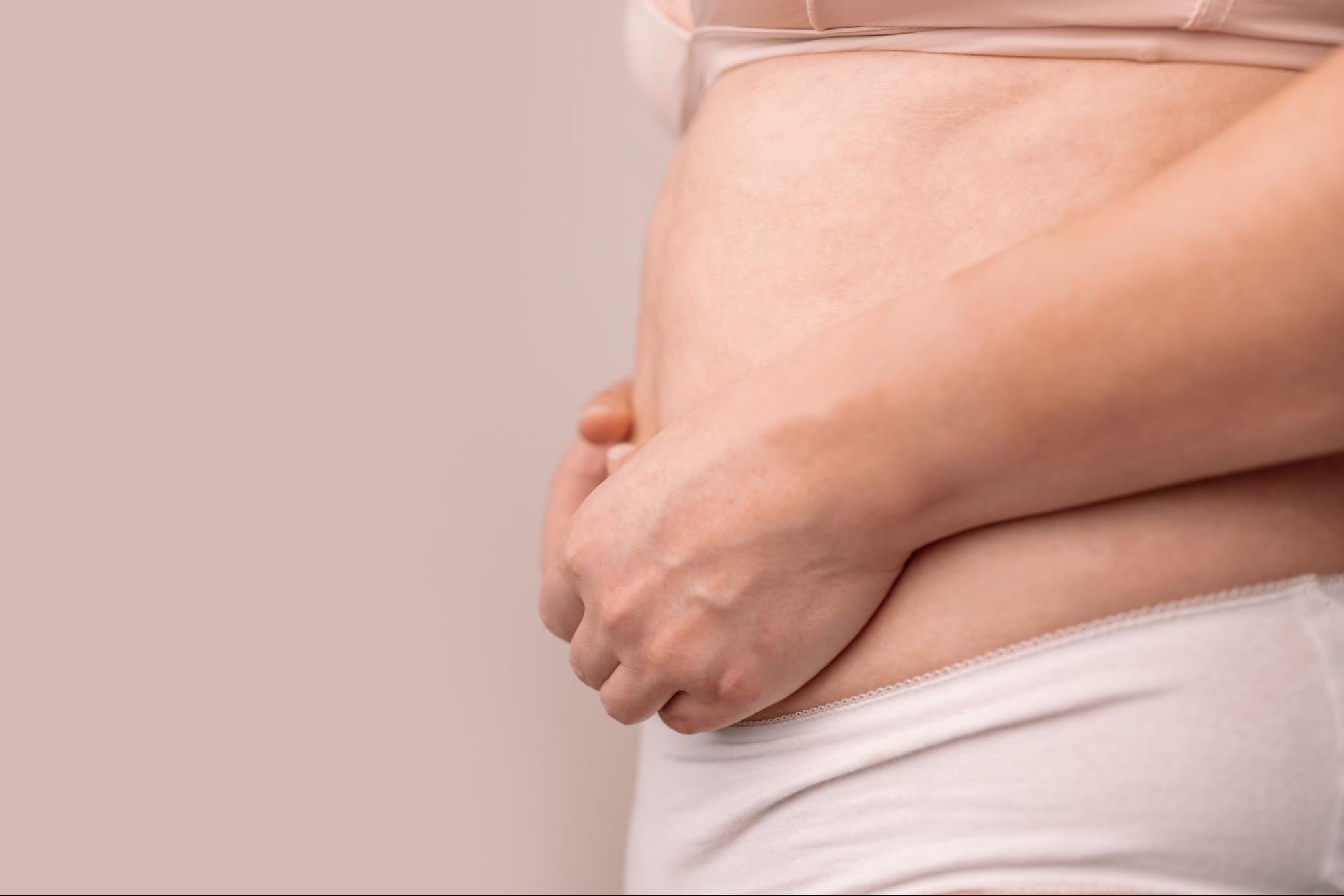 Close-up of a person holding their lower abdomen, representing menopause-related waistline changes (“menobelly”).